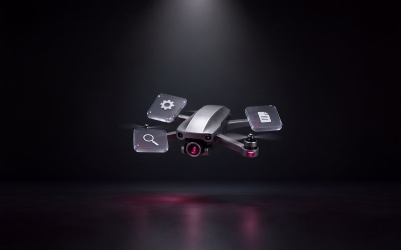 Drone métallique gris en vol stationnaire, objectif de caméra à reflet bordeaux, entouré de trois petites dalles de verre flottantes portant une icône de loupe, d'engrenage et de document, au-dessus d'un sol sombre éclairé par un faisceau blanc