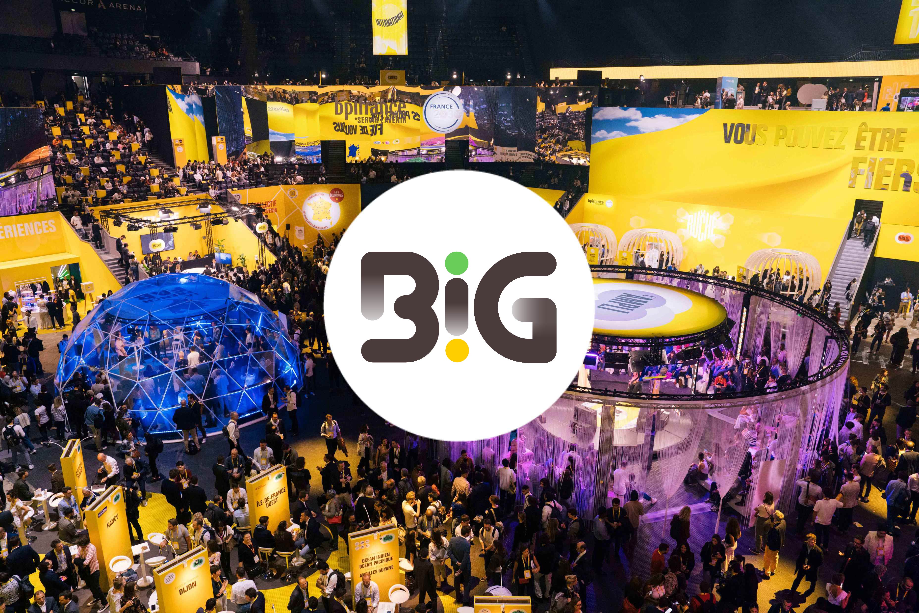 Vue aerienne de l'Accor Arena bondee pendant l'evenement BIG de Bpifrance : au premier plan une foule dense de visiteurs entre des totems jaunes portant des noms de villes (Dijon, Nancy, Ile-de-France Ouest, Ocean Indien), au second plan un dome geodesique bleu eclaire et une structure circulaire violette, a l'arriere-plan les gradins et de grandes banderoles jaunes Bpifrance dont « VOUS POUVEZ ETRE FIERS » ; au centre, le logo « BiG » en lettres brunes dans un cercle blanc