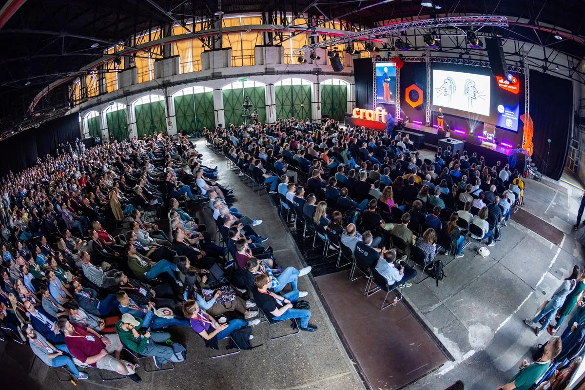 Salle comble vue en plongée fish-eye, centaines de participants assis face à une scène illuminée avec le logo Craft et éclairage coloré