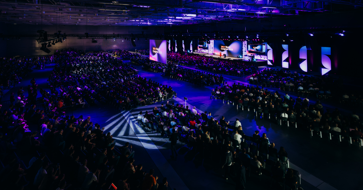 Grande salle de congrès éclairée en bleu, scène centrale avec écrans géants, public nombreux dans l'obscurité au CityCube Berlin
